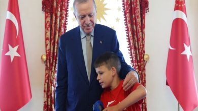 Cumhurbaşkanı Erdoğan ayakta bulunmaktadır, ay yıldızlı kırmızı tişört giyen hoşgörü temsilcisi otizmli çocuk Joshua Harris'in omuzuna dokunuyor.