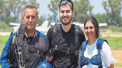 Görselde, açık alanda paraşüt atlayışı öncesinde çekilmiş bir hatıra karesi yer alıyor. Ortada paraşüt ekipmanlarını kuşanmış genç bir kişi, iki eğitmenle birlikte objektife gülümseyerek poz veriyor. Üçünün de üzerinde tandem atlayışa uygun emniyet kemerleri bulunurken, arka planda pist ve küçük uçaklar görülüyor.