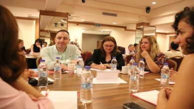Görselde, toplantı salonunda yuvarlak bir masa etrafında oturan katılımcılar erişilebilirlik ve engelli hakları konusunda görüş alışverişinde bulunuyor. Masada su şişeleri, not defterleri ve telefonlar yer alırken, bir katılımcı not alıyor, diğerleri ise dikkatle tartışmayı takip ediyor.