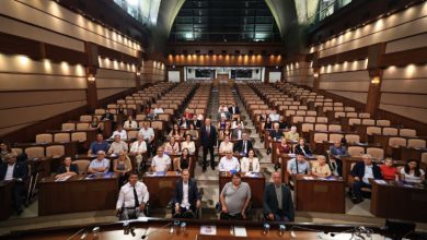 Saraçhane İBB Meclis Salonu'nda, Başkan Vekili Nuri Aslan ayakta bulunurken, kurum yöneticileri ve engelli derneklerin temsilcileri meclis sandalyelerinde oturarak hatıra fotoğrafı veriliyor.