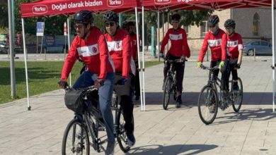 Görselde, kırmızı-beyaz formalar ve kasklar giyen tandem bisiklet sürücüleri, kırmızı çadırların önünden toplu halde hareket ediyor. Önde görme engelli sporcular ve onlara eşlik eden pilot sürücüler yer alırken, etkinlik açık havada gerçekleştiriliyor.