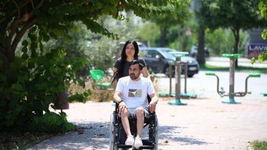Mert Mutluay tekerlekli sandalyede oturuyor ve eşi sokakta aracını sürüyor.