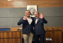 Otizmli yüzücü Tuna Tunca ve Eski Spor Bakanı Dr. Mehmet Kasapoğlu, ayakta yan yana durarak el sallıyor.