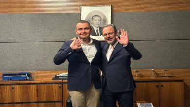 Otizmli yüzücü Tuna Tunca ve Eski Spor Bakanı Dr. Mehmet Kasapoğlu, ayakta yan yana durarak el sallıyor.