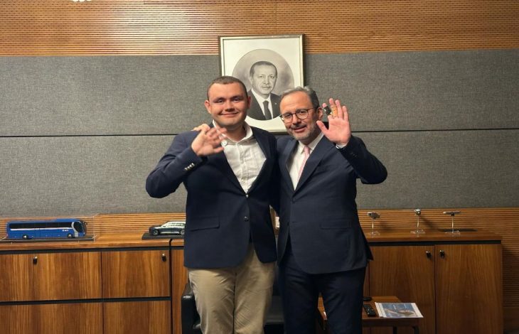 Otizmli yüzücü Tuna Tunca ve Eski Spor Bakanı Dr. Mehmet Kasapoğlu, ayakta yan yana durarak el sallıyor.