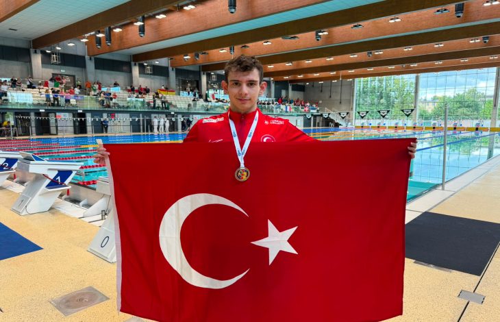 Özel Sporcu Bilge Kağan Yılgın, boynunda madalyası ve elinde Türk bayrağı tutarak poz veriyor.