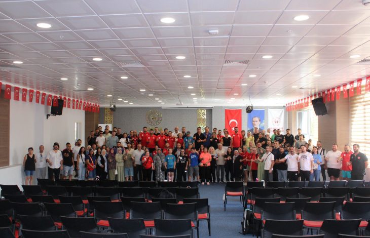 Toplantı salonunda yöneticiler ve sporcular sahnede birlikte anı pozu veriyor.