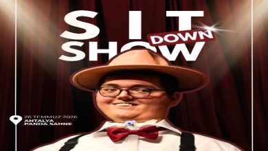 Görselde, kırmızı tiyatro perdesi fonu önünde şapka, papyon ve askılı kıyafet giyen bir kişi gülümseyerek poz veriyor. Afişte "Sit Down Show" başlığı, gösterinin 26 Temmuz 2026'da Antalya Panda Sahne'de gerçekleştirileceği bilgisi yer alırken, sahne ışıkları ve tasarım gösteri atmosferini yansıtıyor.