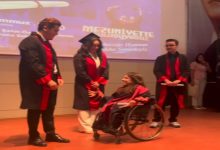 Görselde, mezuniyet töreni sırasında sahnede yaşanan bir an yer alıyor. Tekerlekli sandalye kullanan mezun bir kadın, akademik cübbe giymiş üç kişiyle birlikte sahnede bulunuyor. Mezuniyet cübbeleri içindeki katılımcılar tebessüm ederken, arka planda törene ait projeksiyon ekranı görülüyor.
