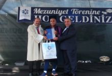 Otizmli Milli Kayakçı Muhsin Murat Bingül'e tören sahnesinde, sağında ve solunda bulunan yetkili erkekler diplomasını takdim ediyor.