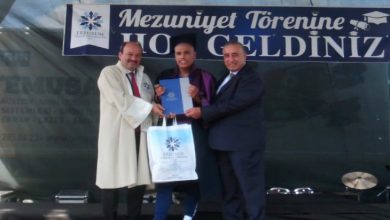 Otizmli Milli Kayakçı Muhsin Murat Bingül'e tören sahnesinde, sağında ve solunda bulunan yetkili erkekler diplomasını takdim ediyor.