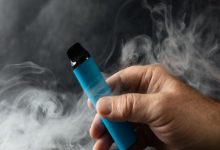 Dumanlar içinde elde tutulan mavi elektronik sigara.