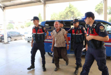 Fotoğrafta, jandarma ekipleri tarafından bulunan Uğur Okuducu iki görevlinin eşliğinde yürürken görülüyor. Arka planda bir jandarma aracı bulunurken, ekipler sağlık kontrolü ve işlemler için kendisini binaya götürüyor.