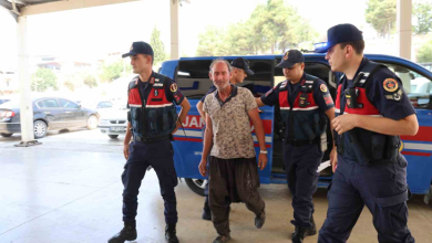 Fotoğrafta, jandarma ekipleri tarafından bulunan Uğur Okuducu iki görevlinin eşliğinde yürürken görülüyor. Arka planda bir jandarma aracı bulunurken, ekipler sağlık kontrolü ve işlemler için kendisini binaya götürüyor.