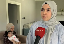 Görselde, açık renk başörtülü bir kadın DHA mikrofonuna konuşuyor. Arka planda koltukta oturan başka bir kadın, kucağında bir bebeği tutuyor.