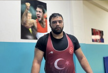 Fotoğrafta, işitme engelli milli güreşçi Berke Nergiz antrenman salonunda görülüyor. Nergiz, üzerinde Türk bayrağı ve ay-yıldız bulunan kırmızı güreş mayosuyla kameraya poz veriyor. Arka plandaki duvarda bir güreşçinin müsabaka sırasında çekilmiş büyük bir fotoğrafı yer alıyor. Haber, Berke Nergiz'in Avrupa'da başarı elde etme hedefini konu alıyor.