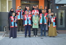 Fotoğrafta Vefa Sosyal Destek Ekibi üyeleri, yaşlı ve engelli bireylerle birlikte bir kamu binasının girişinde toplu halde objektife poz veriyor. Ekip üyeleri üzerlerinde görev yelekleriyle yer alırken, bina girişinde erişilebilirlik işareti de görülüyor.