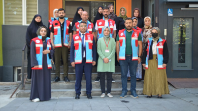 Fotoğrafta Vefa Sosyal Destek Ekibi üyeleri, yaşlı ve engelli bireylerle birlikte bir kamu binasının girişinde toplu halde objektife poz veriyor. Ekip üyeleri üzerlerinde görev yelekleriyle yer alırken, bina girişinde erişilebilirlik işareti de görülüyor.