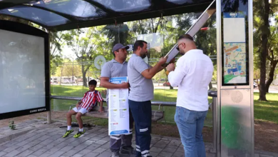 Görselde belediye görevlileri, bir otobüs durağında erişilebilirlik çalışması yaparken görülüyor. Durakta bilgilendirme panoları ve oturan bir çocuk bulunuyor.