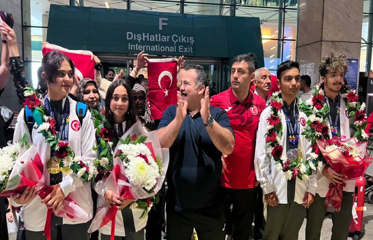 Türkiye İşitme Engelliler Spor Federasyonu Başkanı Dursun Gözel ile milli sporcular, çiçek ve Türk bayrakları tutarak yan yana duruyor.