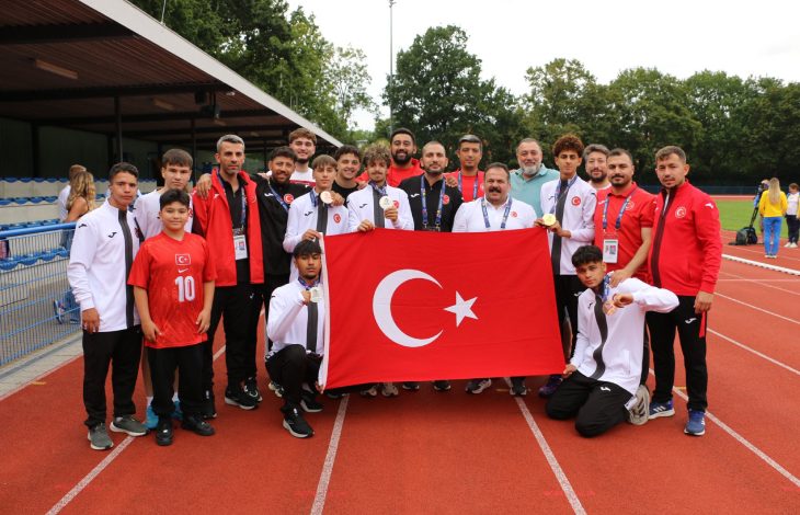 İşitme Engelliler Atletizm Takımı Milli Sporcuları, teknik kadro ile Türkiye İşitme Engelliler Spor Federasyonu Başkanı Dursun Gözel pistte Türk bayrağı tutarak poz veriyor.