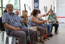 Bir salonda yan yana oturan görme engelli bireyler, ellerinde farklı türlerde beyaz bastonlar tutarken görülüyor.