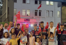 Görselde jandarma personeli, çocuklar ve aileleri bir jandarma binasının önünde Türk bayraklarıyla toplu halde poz veriyor.