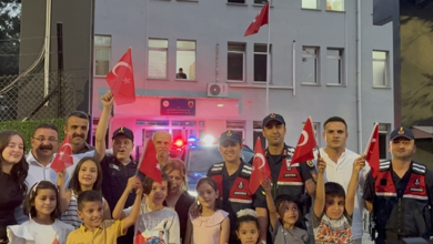 Görselde jandarma personeli, çocuklar ve aileleri bir jandarma binasının önünde Türk bayraklarıyla toplu halde poz veriyor.