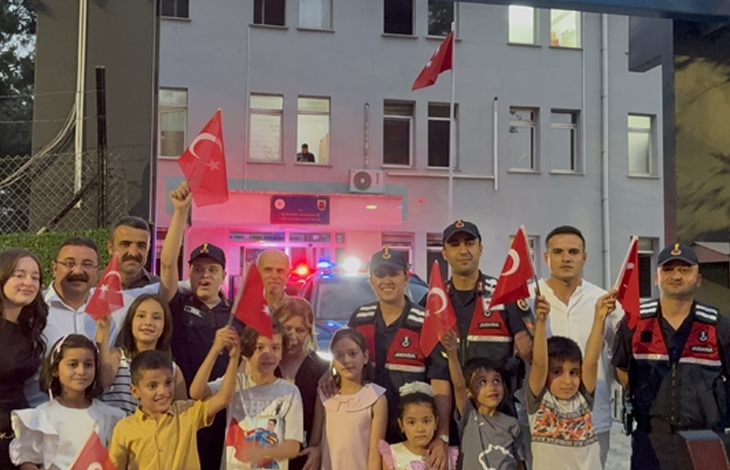 Görselde jandarma personeli, çocuklar ve aileleri bir jandarma binasının önünde Türk bayraklarıyla toplu halde poz veriyor.