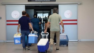 Fotoğrafta, birkaç sağlık çalışanı ve kişi, ellerinde ve taşıma arabalarında soğuk muhafaza kutuları taşırken görülüyor.