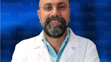 Fotoğrafta Doç. Dr. Ümit Alakuş, beyaz hekim önlüğü giymiş, sakallı ve gözlüklü bir erkek. Kollarını göğsünde birleştirmiş şekilde duruyor. Üzerindeki önlükte “Egepol Hastaneleri” logosu bulunuyor. Arka planda aynı logonun tekrarlandığı mavi bir tanıtım panosu var. Doktor, profesyonel ve güven veren bir ifadeyle gülümsüyor.