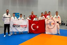 Down Judo Millî Takımı sporcuları ile teknik heyet, Türk Bayrağı, Spor Toto, TÖSSFED flamalarını tutarak spor salonunda poz veriyor.