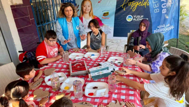 Çocuklar ve yetişkinler, açık alanda kurulan masanın etrafında çeşitli etkinlik malzemeleriyle çalışma yapıyor.