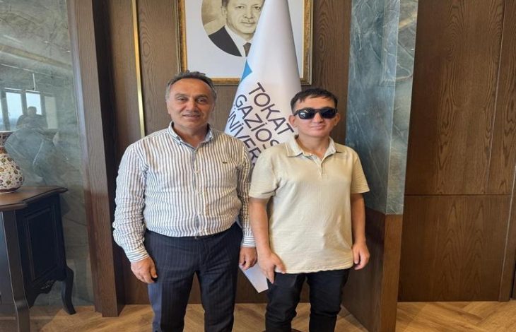 Görme engelli öğrenci Taha Gül, Tokat Gaziosmanpaşa Üniversitesi Rektörü Prof. Dr. Fatih Yılmaz ile beraber yan yana poz veriyor.