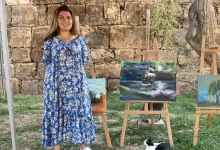 Ayşe Işık, açık alanda sergilenen tablolarının yanında ayakta duruyor.
