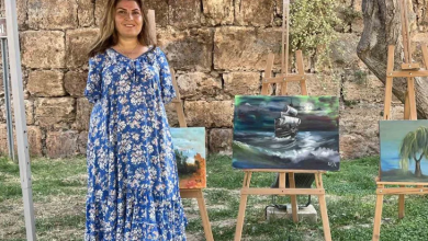 Ayşe Işık, açık alanda sergilenen tablolarının yanında ayakta duruyor.
