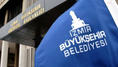 Bir binanın önünde mavi renkli "İzmir Büyükşehir Belediyesi" yazan bayrak var. Binanın üstündeki yazı tam olarak seçilmiyor.