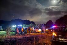 Gece saatlerinde kırsal alanda, ekipler ve vatandaşlar araçların ışıkları altında arama çalışması yürütüyor.