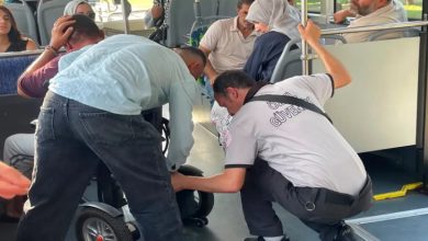 Kaza geçiren engelli yolcu başını tutarken, ön planda iki erkek yolcu akülü sandalye aracına müdahale ediyor.