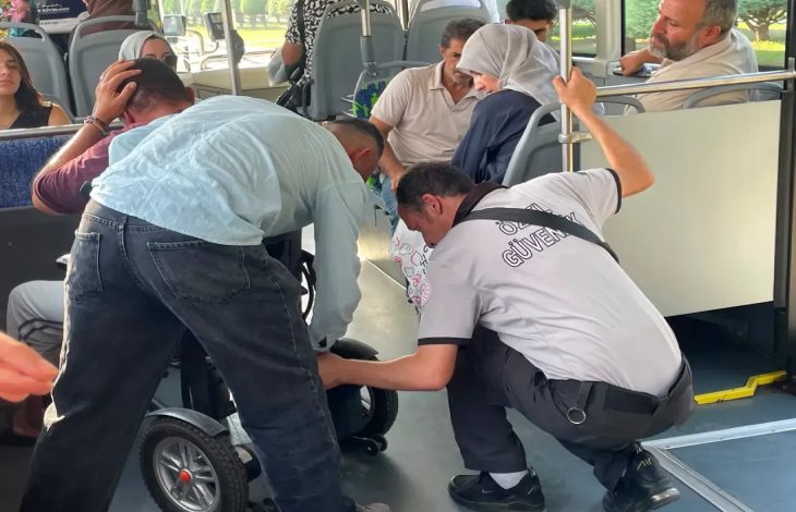 Kaza geçiren engelli yolcu başını tutarken, ön planda iki erkek yolcu akülü sandalye aracına müdahale ediyor.