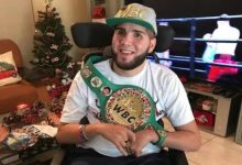 Görselde, boksör Prichard Colón tekerlekli sandalyede otururken kameraya doğru gülümsüyor; üzerinde beyaz bir tişört, başında WBC yazılı bir şapka ve omzunda WBC şampiyonluk kemeri bulunuyor. Arka planda süslenmiş bir Noel ağacı ve televizyonda bir boks karşılaşması görülüyor.