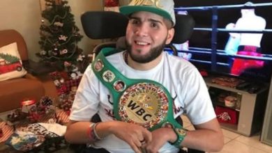 Görselde, boksör Prichard Colón tekerlekli sandalyede otururken kameraya doğru gülümsüyor; üzerinde beyaz bir tişört, başında WBC yazılı bir şapka ve omzunda WBC şampiyonluk kemeri bulunuyor. Arka planda süslenmiş bir Noel ağacı ve televizyonda bir boks karşılaşması görülüyor.