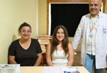 Görselde, bir sınıf ortamında masanın arkasında yan yana oturan iki kadın ile yanlarında beyaz önlükle ayakta duran bir erkek görülüyor. Masanın üzerinde kitaplar ve eğitim materyalleri bulunuyor. Görsel, Mersin’de görme engelli Nisa’nın üniversite hayalinin gerçekleşmesine ilişkin habere ait.