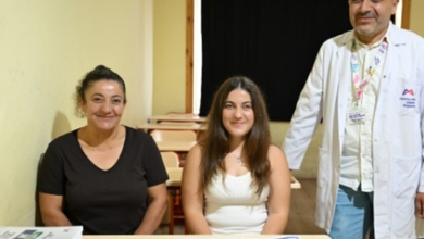Görselde, bir sınıf ortamında masanın arkasında yan yana oturan iki kadın ile yanlarında beyaz önlükle ayakta duran bir erkek görülüyor. Masanın üzerinde kitaplar ve eğitim materyalleri bulunuyor. Görsel, Mersin’de görme engelli Nisa’nın üniversite hayalinin gerçekleşmesine ilişkin habere ait.
