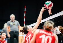 Görselde oturarak voleybol kadınlar müsabakasından heyecanlı bir an görülüyor. Kırmızı forma giyen Türkiye takımı oyuncuları, file önünde rakipleriyle mücadele ediyor. Ön planda sırtında “Türkiye” yazısı ve 10 numarası bulunan bir millî takım oyuncusu dikkat çekiyor. Ortada ise kırmızı formalı başka bir oyuncu, topa müdahale etmek için fileye doğru uzanmış durumda. Rakip takımın oyuncuları da file üzerinde topa karşı hamle yapıyor.