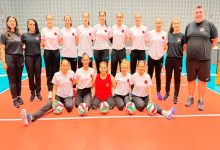 Görselde, kapalı bir spor salonunda Türk kadın oturarak voleybol milli takımının oyuncuları ve teknik ekibi, voleybol toplarıyla birlikte takım fotoğrafı için poz verirken görülüyor.
