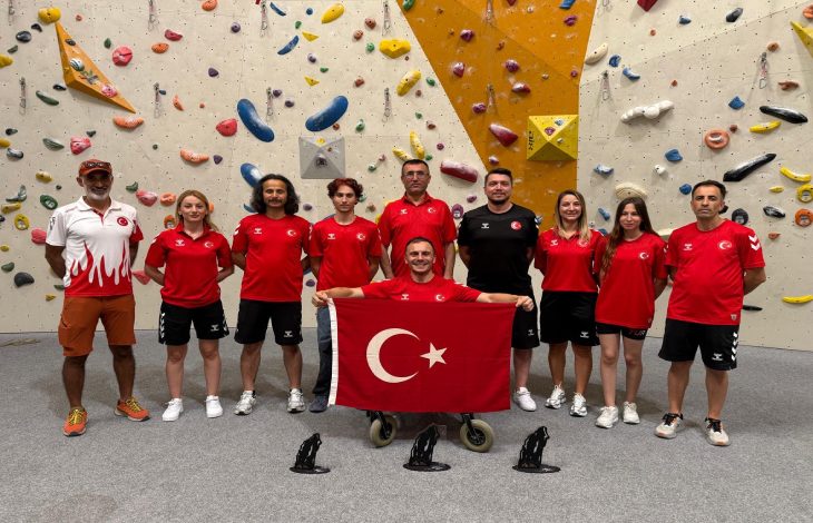 Fotoğrafta, tırmanış duvarının önünde kırmızı-beyaz Türk milli takım formaları giyen bir grup sporcu ve görevli, ortada Türk bayrağı tutan tekerlekli sandalyedeki bir sporcu ile birlikte gururla poz veriyor.