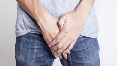 Kot pantolon ve tişört giyimli erkek kişi ağrı olan genital bölgesini eliyle tutuyor.