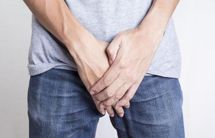 Kot pantolon ve tişört giyimli erkek kişi ağrı olan genital bölgesini eliyle tutuyor.