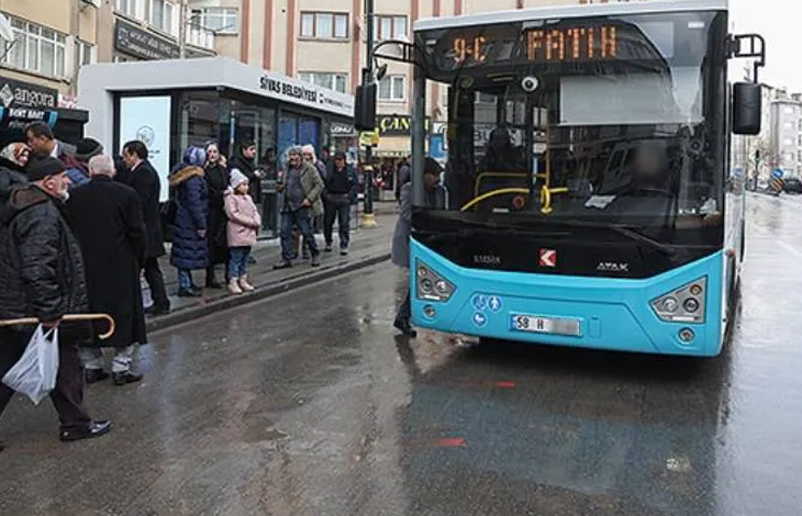 Fotoğrafta, yağışlı havada bir şehir içi otobüsü durakta yolcu almak üzere bekliyor. Durakta otobüsü bekleyen vatandaşlar görülürken, otobüsün ön ekranında "Fatih" hattı yazıyor. Yolda ıslak zemin ve çevredeki binalar dikkat çekiyor.